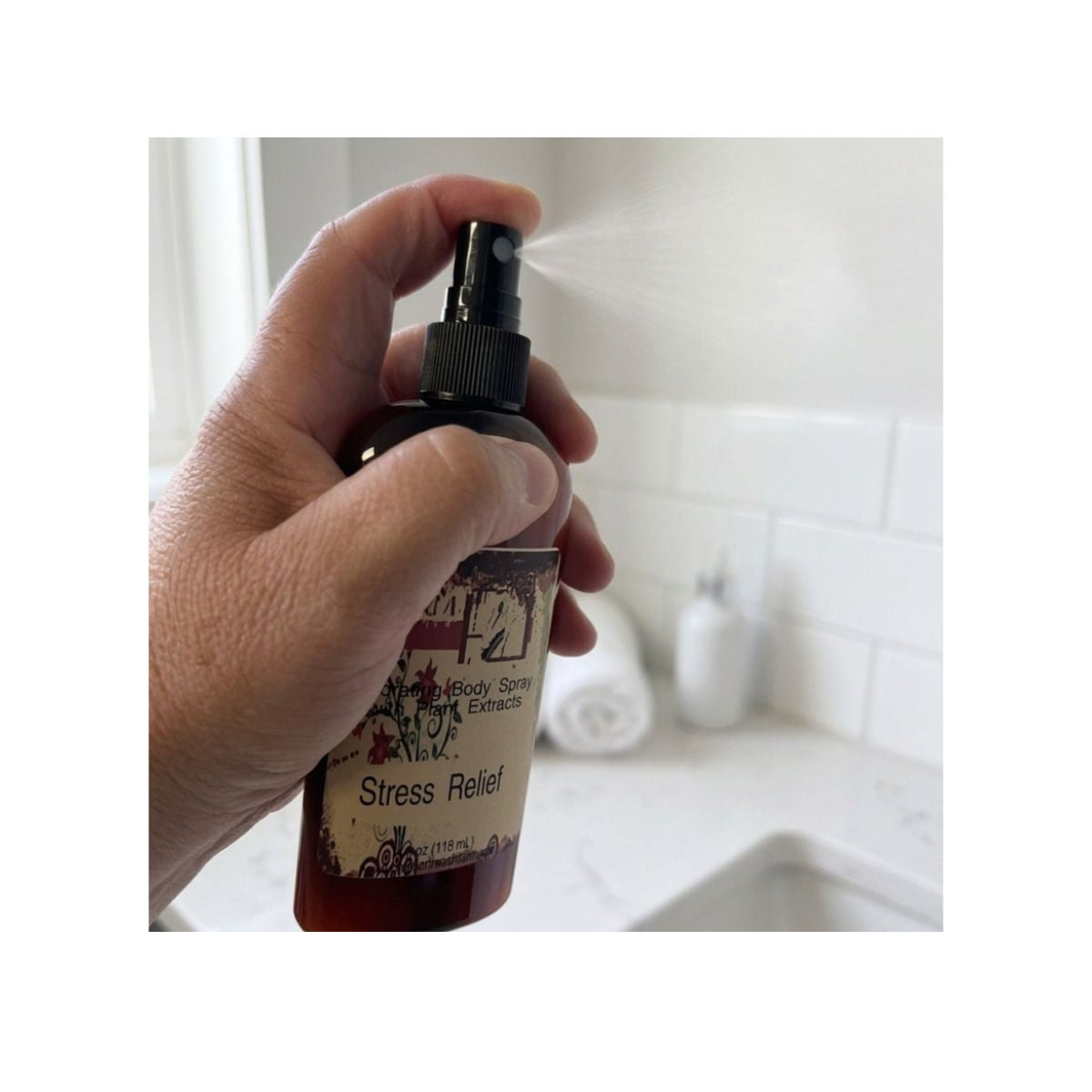 A hand holding and spraying a dark amber bottle labeled 'Scented Stress Relief' body spray, with a bathroom background.