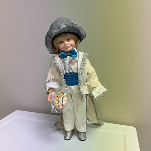 The Robin Woods 1989 Doll Painting Palette 15 inch features a classic white tuxedo and coattail jacket, a striking turquoise bowtie and cummerbund, short blond hair and blue eyes, and a detailed paint palette. Perfect for anyone looking to bring a touch of timeless elegance and creativity to their collection. This vintage collector's doll is in used condition and may need cleaned. There is a spot on the jacket. This item was obtained from an estate sale among many other vintage dolls. 